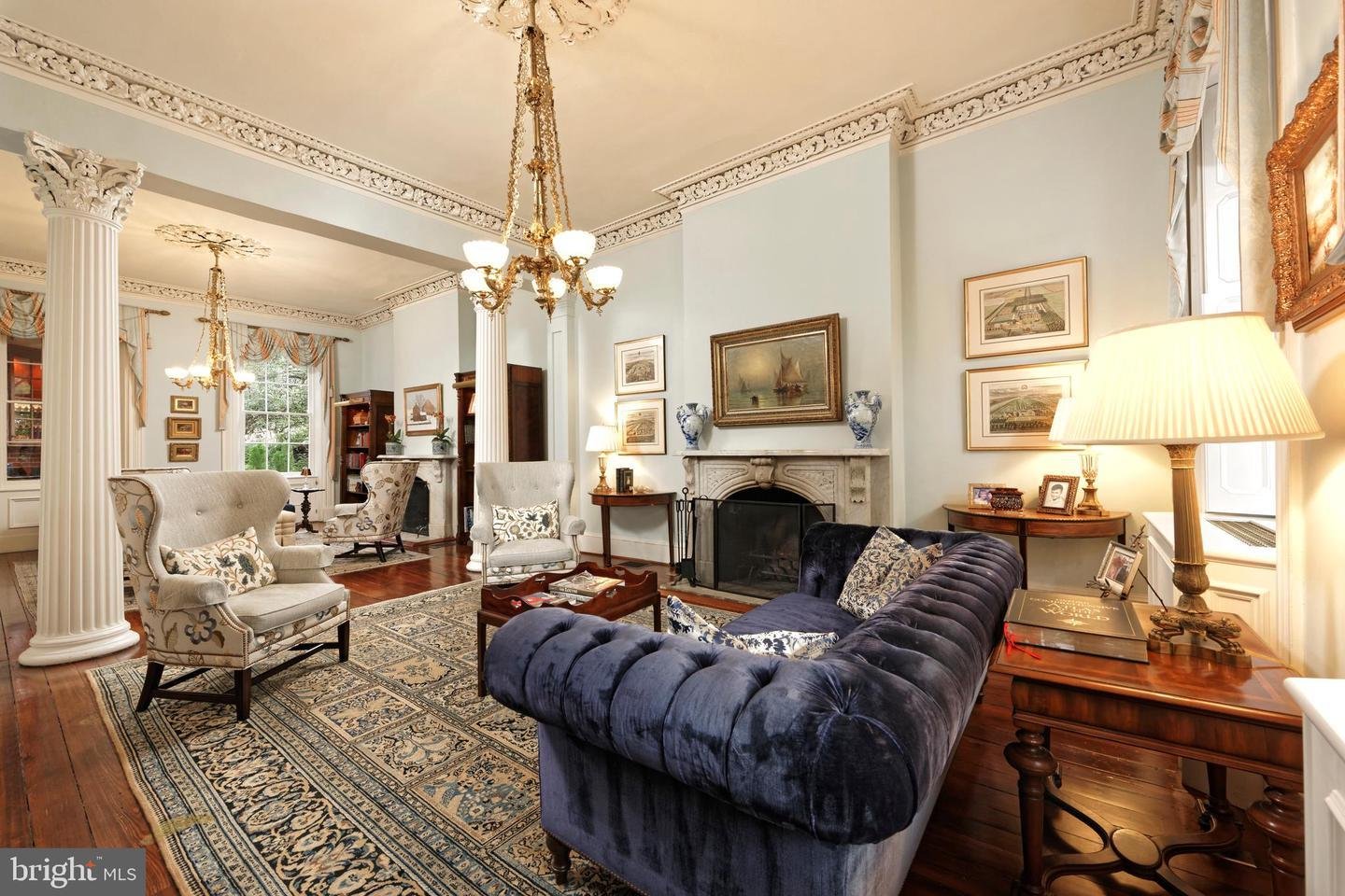 Living room with a blue tufted sofa, marble fireplace, fluted columns, and ornate ceiling molding.