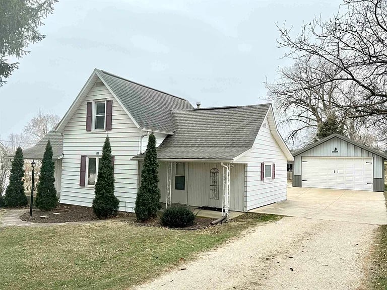 White-sided house with maroon shutters, covered entry, detached garage, and wide driveway.