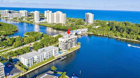 Aerial view of waterfront condos beside an inlet, with a bridge and the Atlantic Ocean beyond.