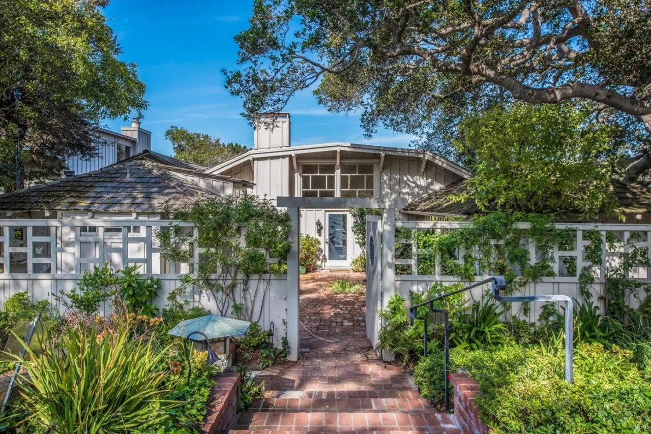 Home entrance framed by mature trees, with a brick walkway and white garden gate.