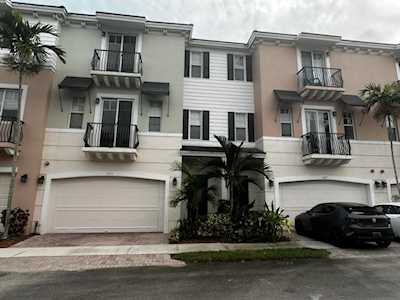 Attached townhomes with pastel facades, balconies, white garage doors, and palm landscaping.