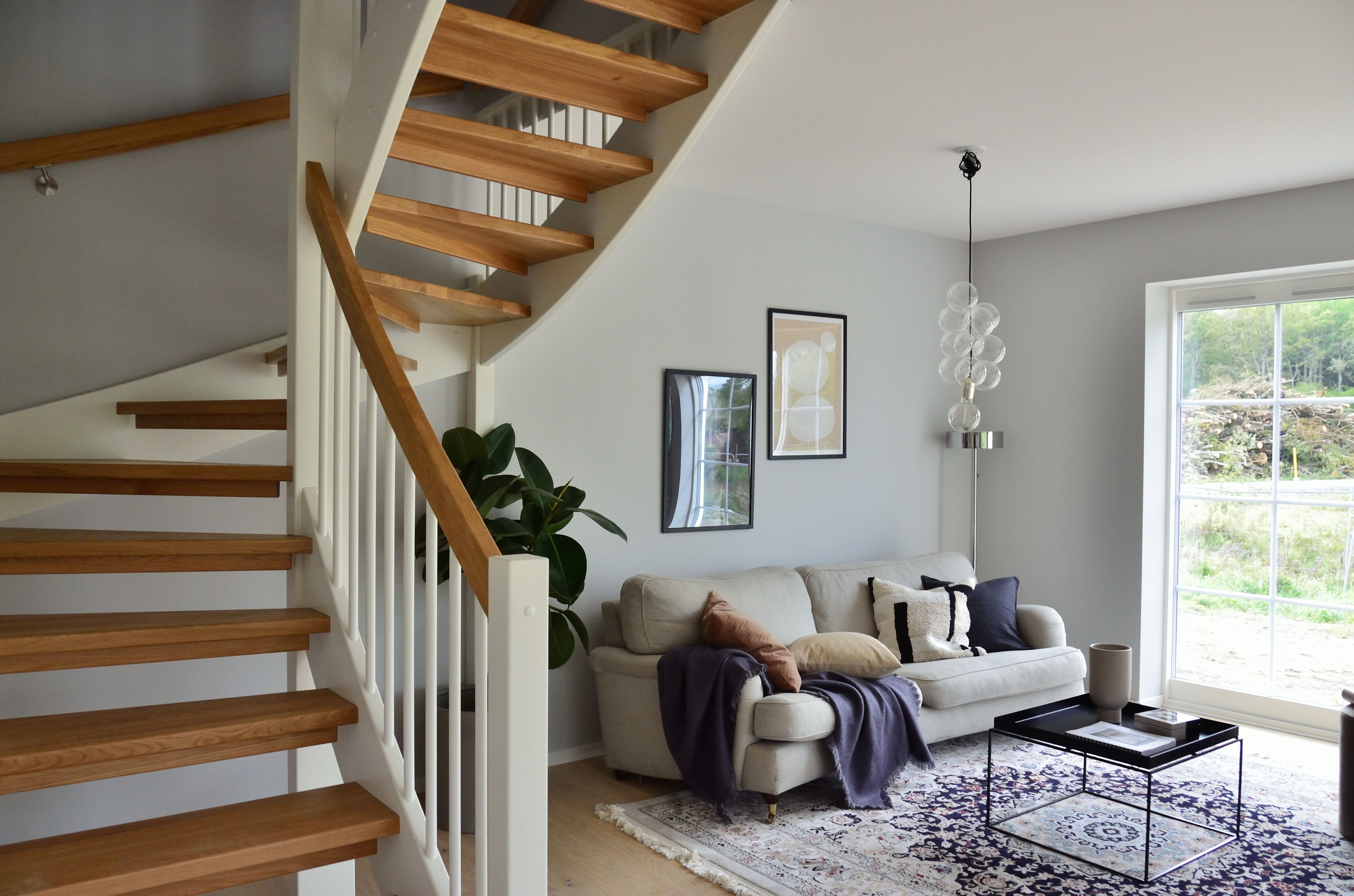 Living room with an open-riser wooden staircase, light sofa, and large window.