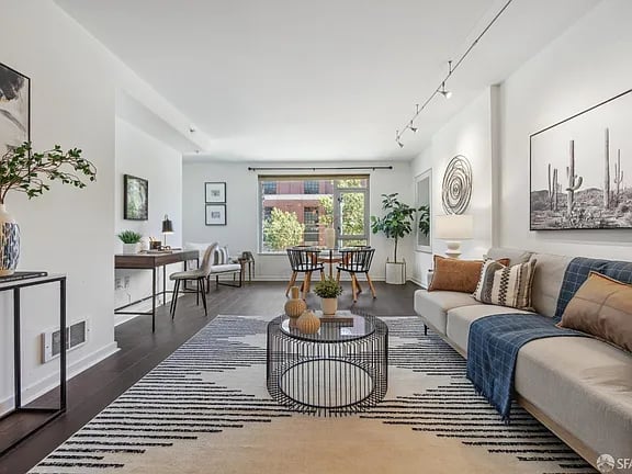 Bright living room with a light sofa, striped rug, and dining area beside large windows.