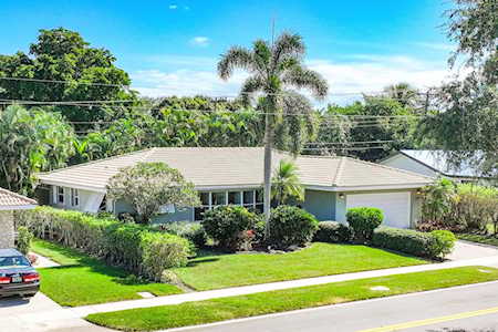 Single-story house with a light roof, clipped hedges, central palm tree, and broad lawn.