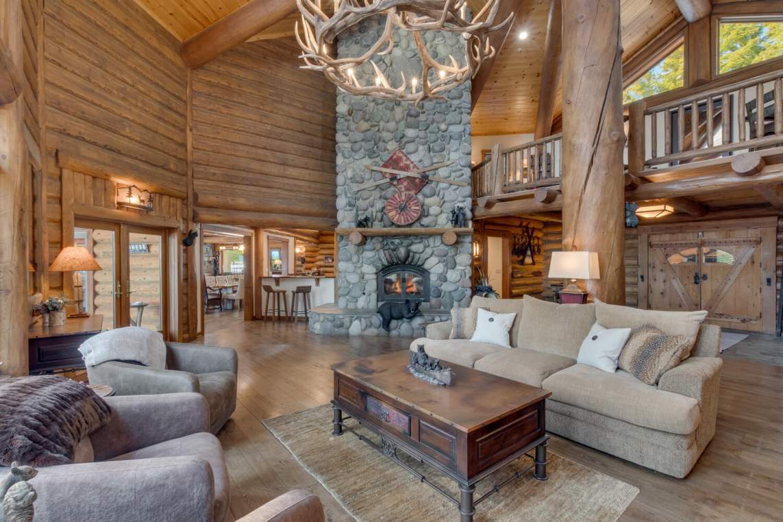 Rustic log-home living room with a towering stone fireplace and vaulted wood ceiling.