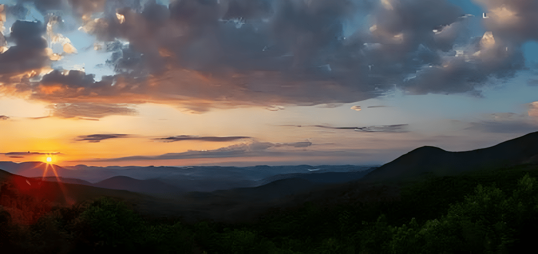 Layered mountain ridges and forested hills beneath sunset clouds.