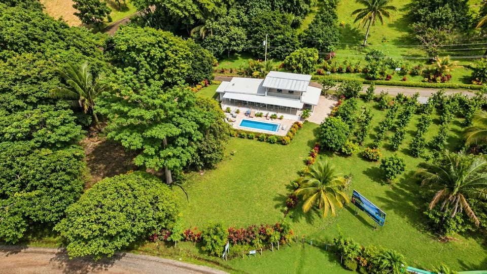 Modern white house and swimming pool amid lush tropical grounds, viewed from above.