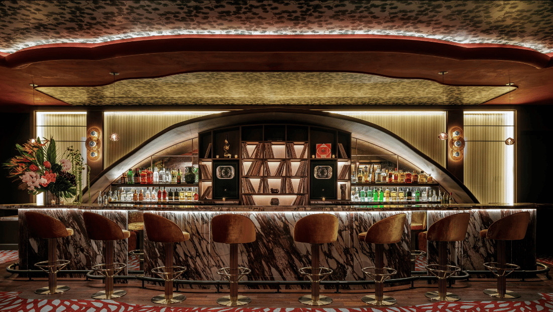Japanese cocktail lounge with a veined-marble bar, brown stools, and illuminated liquor shelves.
