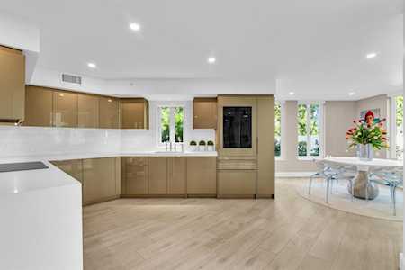Open-plan kitchen with light wood cabinets and a glass dining table beside tall windows.