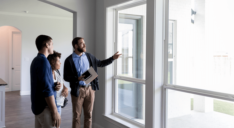 Three people, possibly real estate agent and his clients, looking out of a window and discussing something. They are indoors, and the setting appears professional.