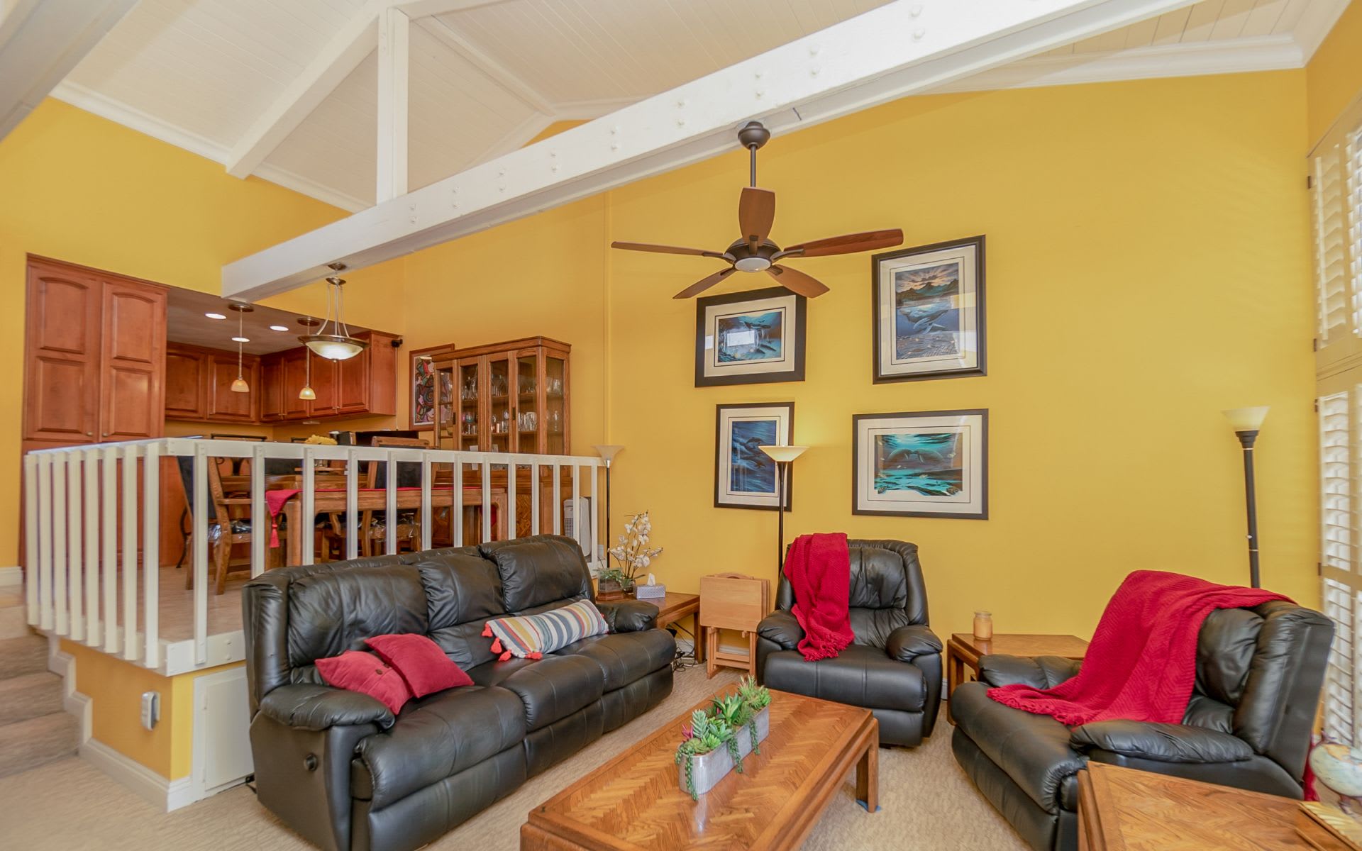 Living room with vaulted white-beamed ceiling, yellow walls, and black leather seating.