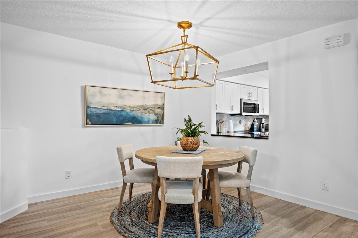 Condominium dining area with a round table, woven rug, brass pendant, and kitchen opening.