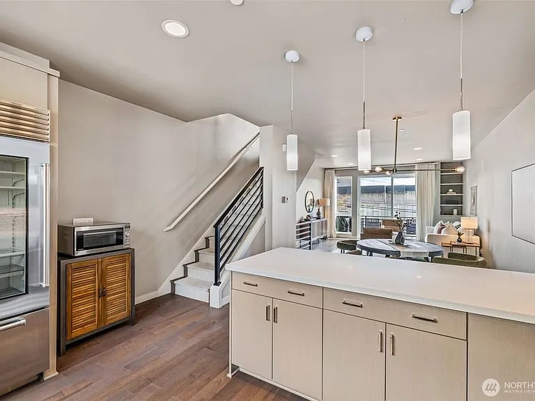 Open-plan kitchen with a large white island, wood floors, and a black-railed staircase.