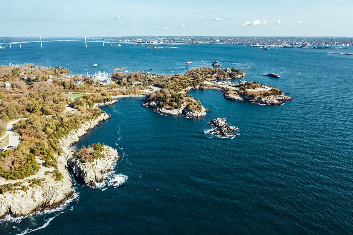 Aerial view of Jamestown’s rocky, wooded coastline, with boats offshore and a bridge across the bay.
