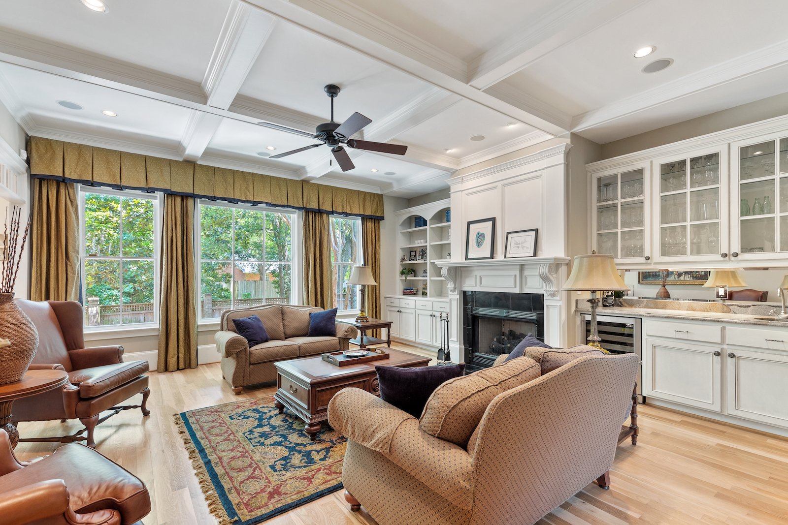 Living room with a coffered ceiling, built-in fireplace, large windows, and leather and upholstered seating.