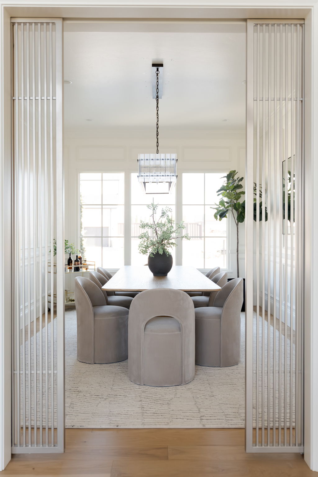 Bright dining room with a light-wood table, upholstered chairs, and large windows.
