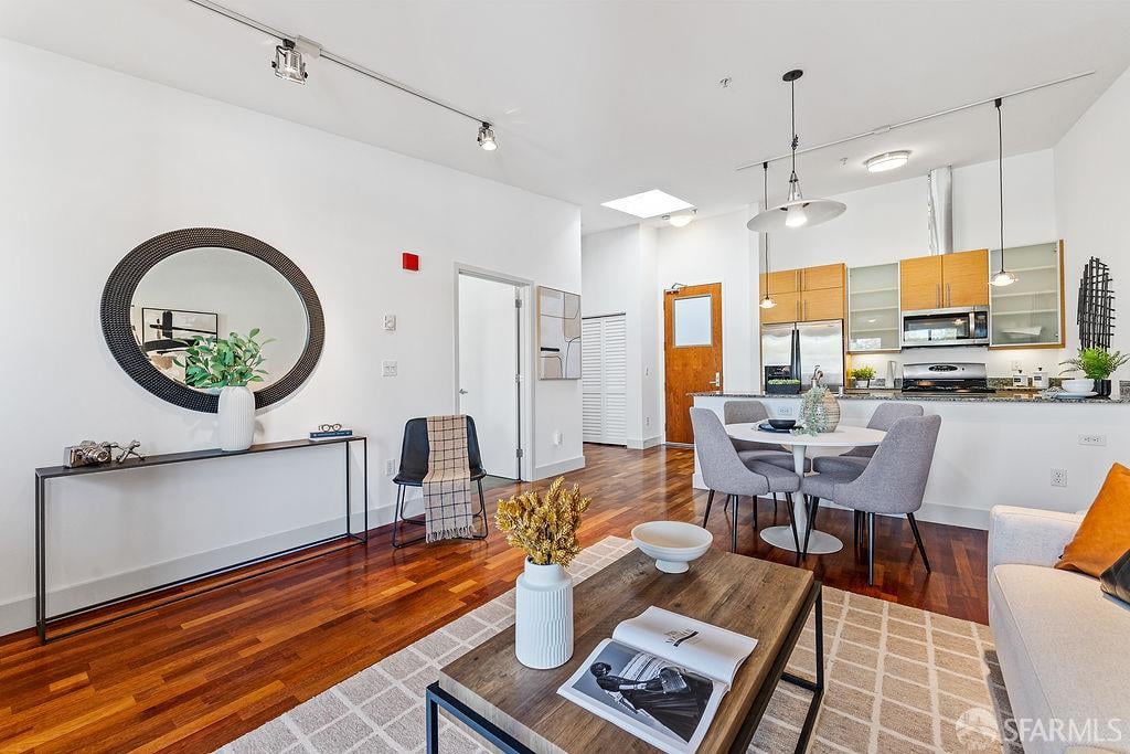 Open-plan condo living room with hardwood floors, dining area, and light wood kitchen cabinets.