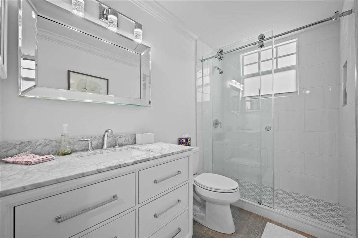 Bathroom with marble-topped white vanity and glass shower with patterned tile floor.