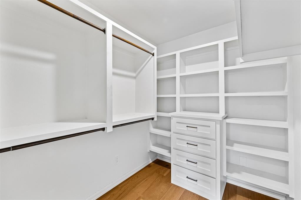 Walk-in closet with white built-in shelving, hanging rods, and a central stack of drawers.