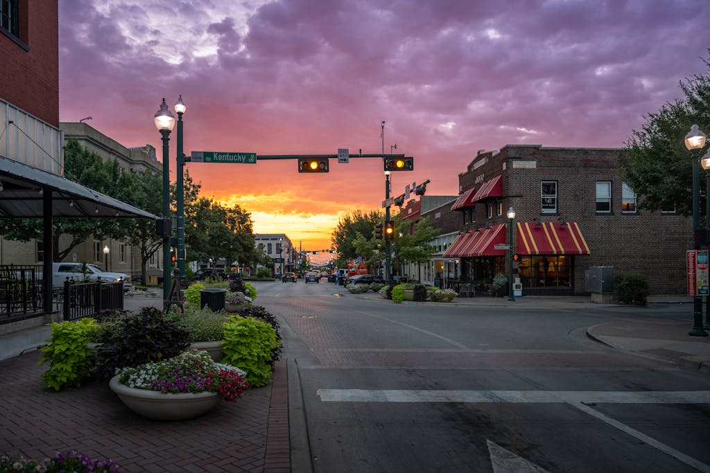 Downtown McKinney storefronts and landscaped planters beneath a colorful sunset sky.