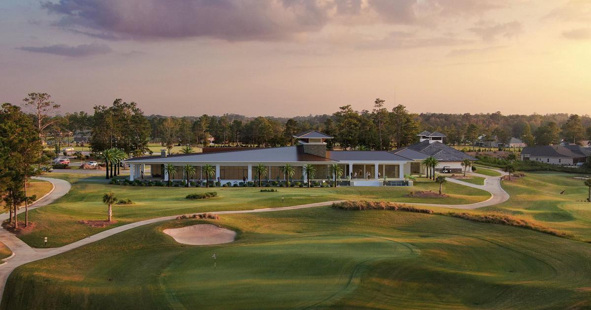 Golf course clubhouse beside a putting green and sand bunker in warm evening light.