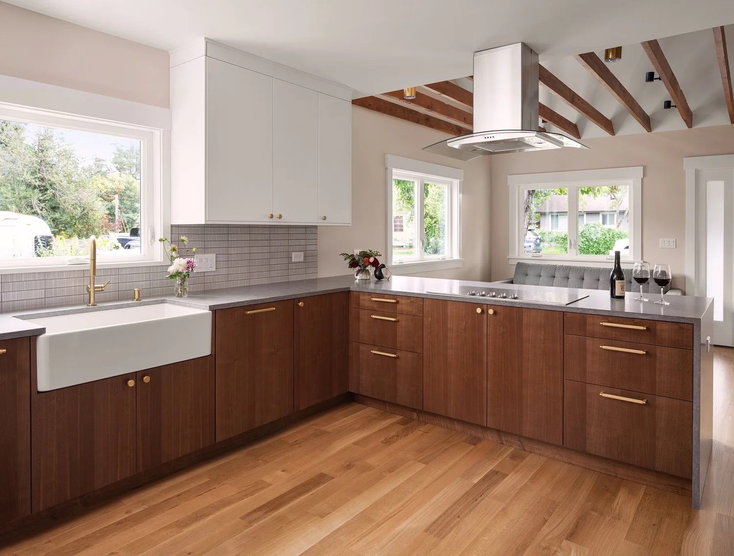 A kitchen with rift walnut slab base cabinets and drawers, brass bar pulls, white upper cabinets, a white apron sink, and a gray waterfall-edge peninsula.