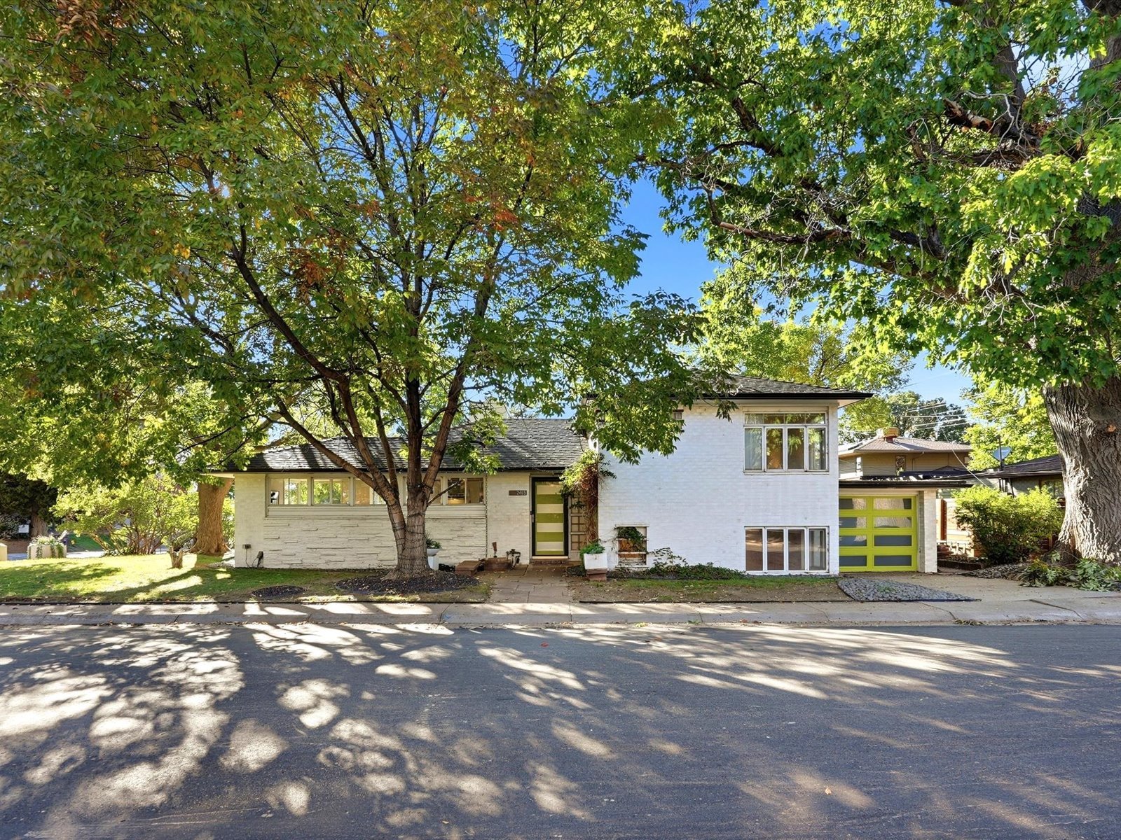 White-brick mid-century modern home framed by mature trees, with a lime-green garage door.