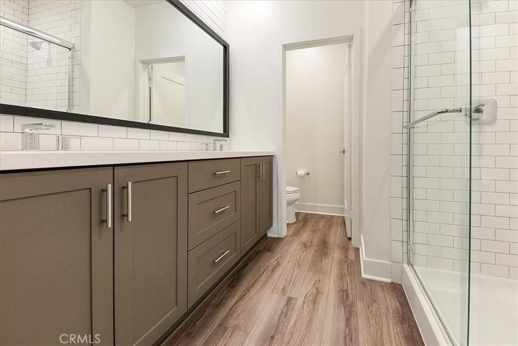  A modern bathroom with light gray cabinets, a large mirror, and a walk-in shower with subway tile.