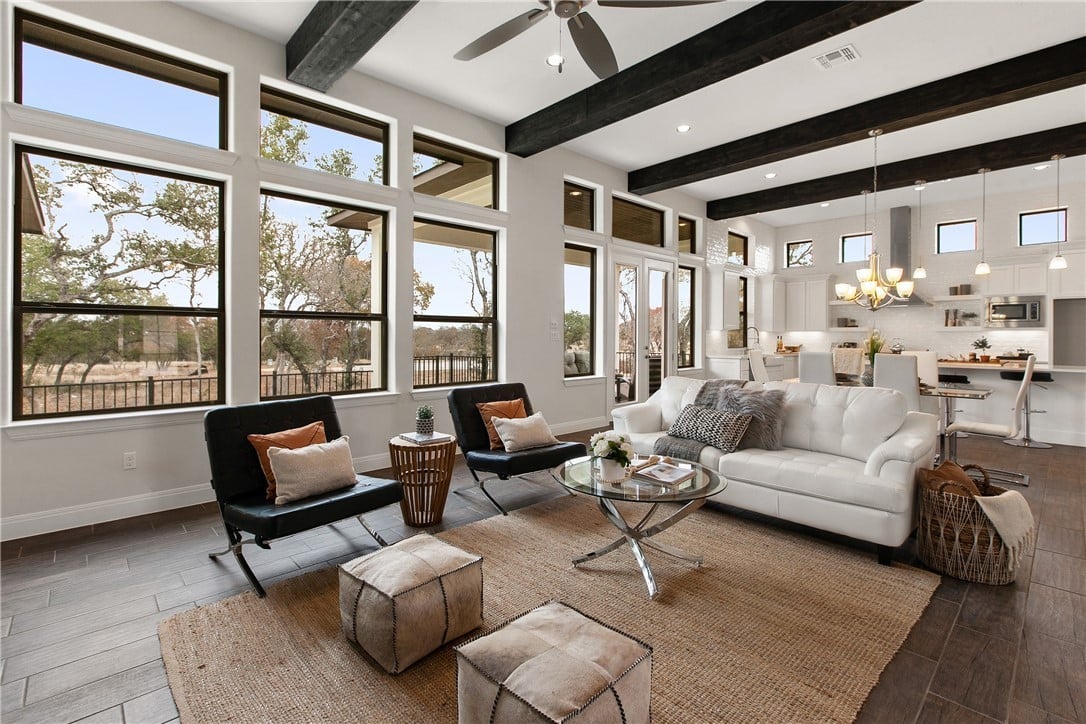 Bright living room with exposed beams, tall windows, a white sofa, and an open kitchen.