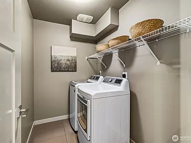 Laundry room with white front-loading washer and dryer beneath a wire shelf with woven baskets.