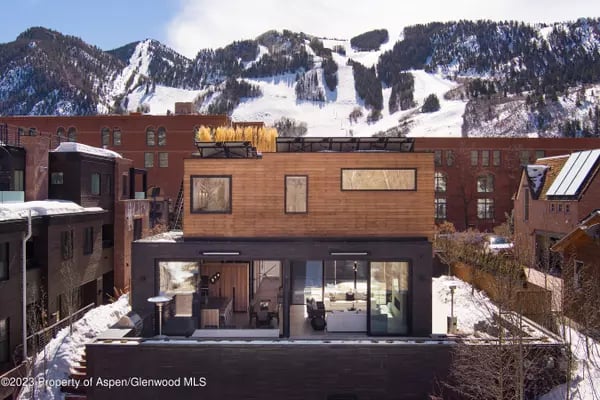 Modern Aspen home with wood exterior and large glass doors, backed by snow-covered mountains.