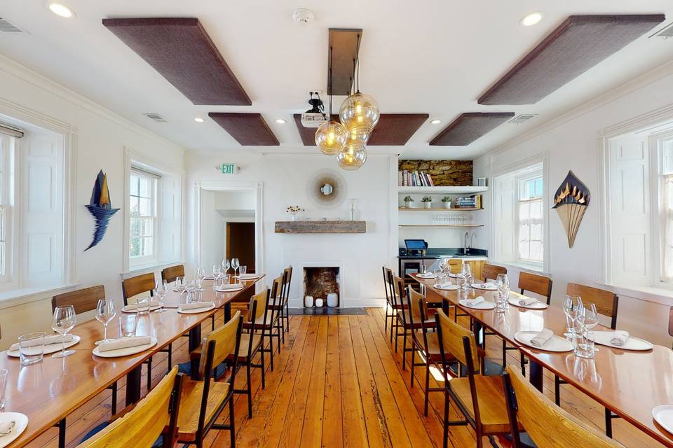 Private dining room at Field & Main in Marshall, VA with long wooden farm tables set for a group, wide-plank pine floors, a brick fireplace and globe pendant lights