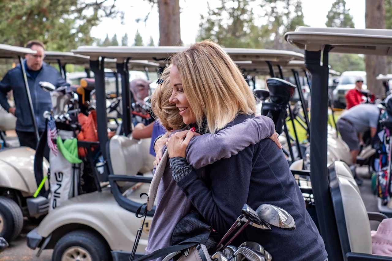 Two women hug beside golf carts at an outdoor gathering.