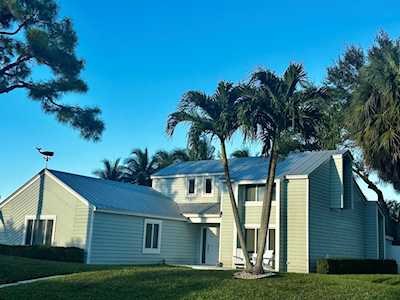 Light-colored home with a blue-gray roof, palm trees, and a broad green lawn.