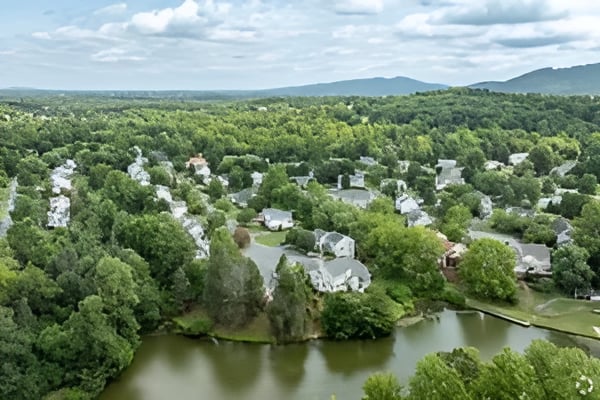 Aerial view of homes among wooded hills, with a pond in the foreground and mountains beyond.