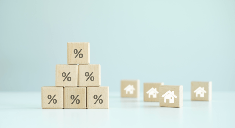 Wooden percentage blocks beside miniature house tokens, illustrating real estate rates.