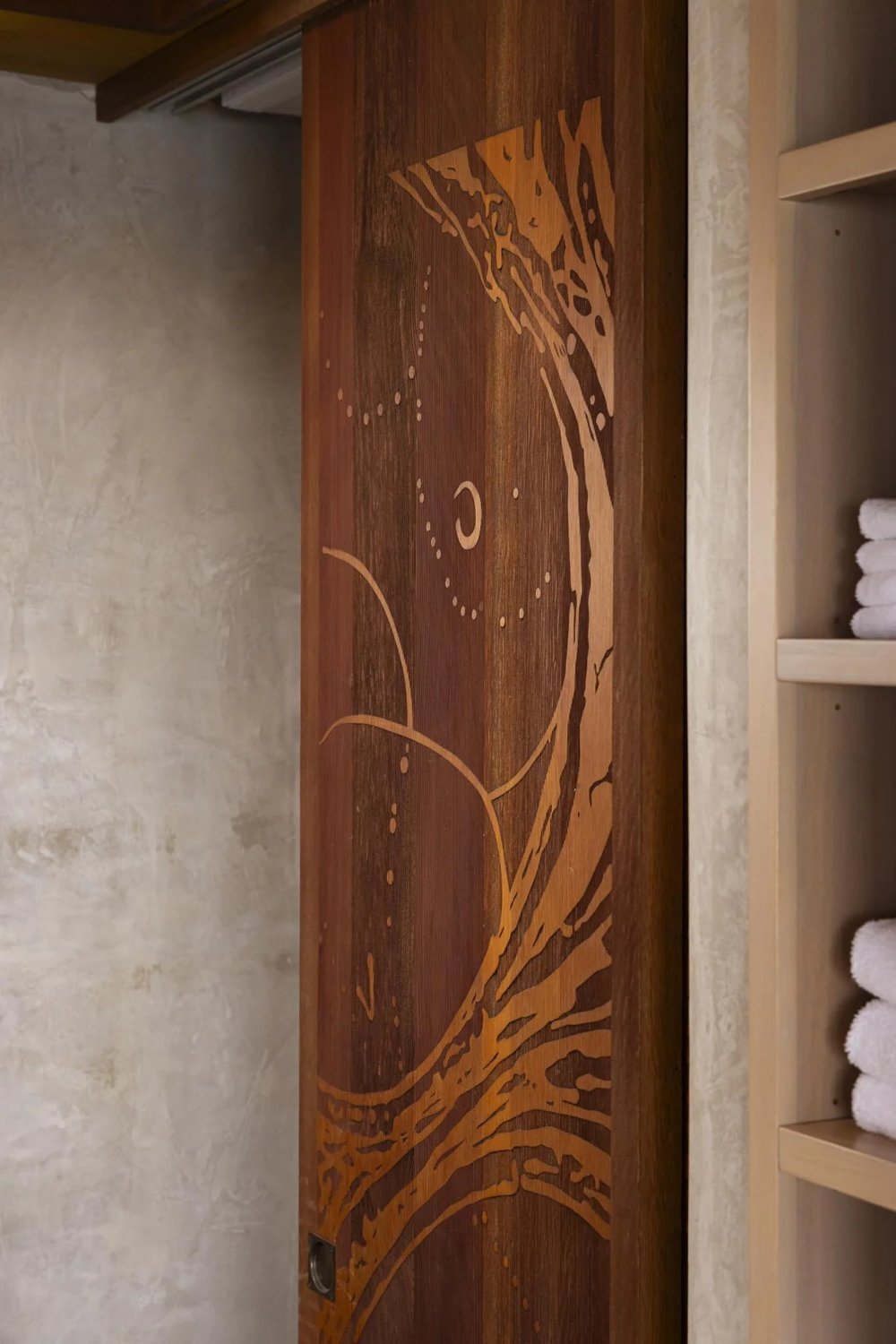 A tall wood interior door in the upstairs suite with a flowing inlaid pattern in contrasting wood tones.
