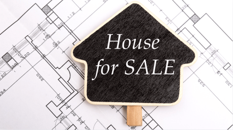 House-for-sale sign resting on architectural blueprints.