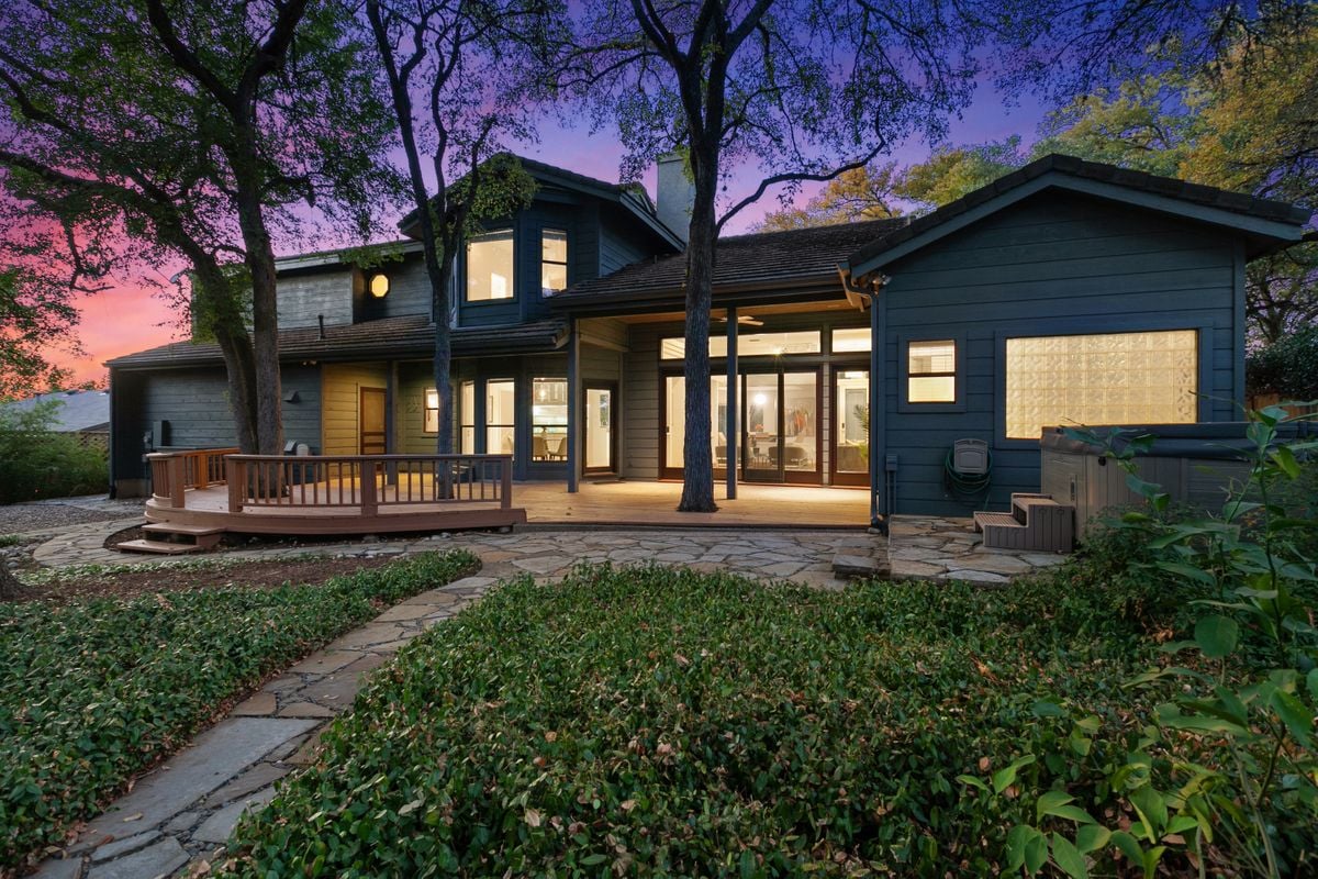 Twilight rear elevation of this modern home at 2131 Barton Hills Drive, Austin, TX 78704, with a wood deck and stone patio lit against a dusk sky. Built by Wilde Custom Homes, Barton Hills.