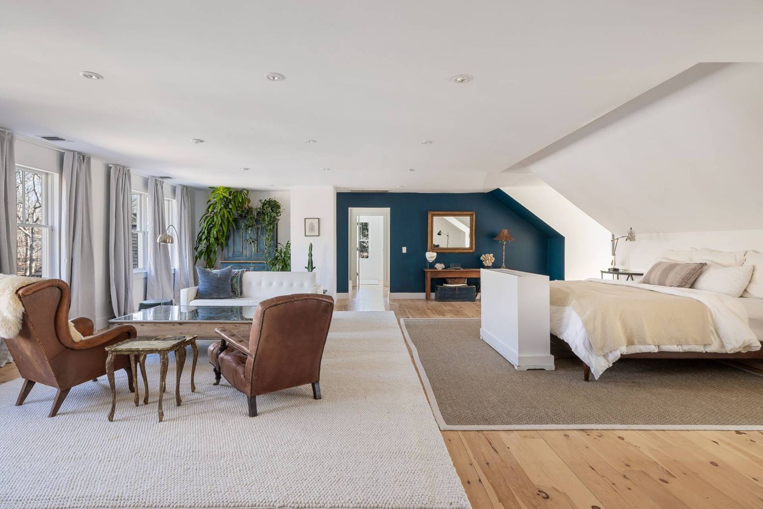 Bedroom and sitting area with a white bed, brown leather chairs, and a deep blue accent wall.