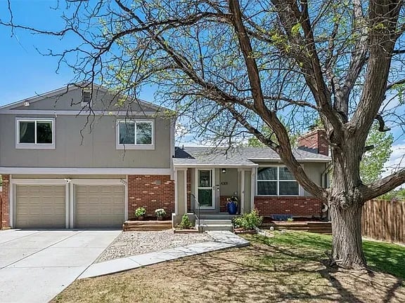 Two-story home with a two-car garage, red brick facade, and large tree in the front yard.