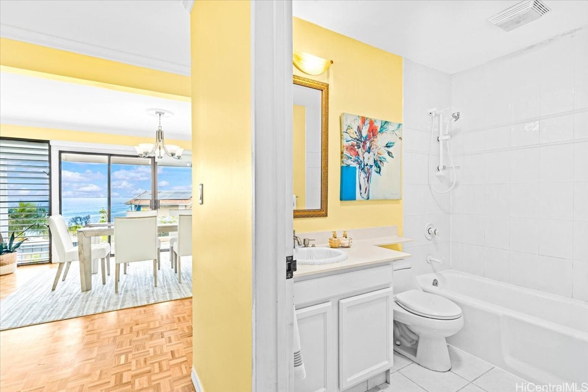 Bathroom with a white tub and vanity; dining area and ocean view visible through the doorway.