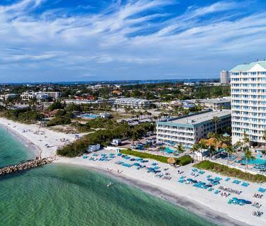Aerial view of Lido Key shoreline with beach umbrellas, turquoise water, and beachfront buildings.