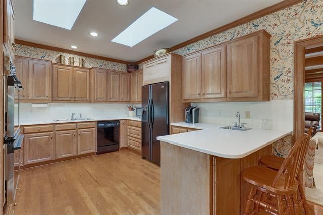 Kitchen with light wood cabinetry, a white peninsula, bar stools, and skylights.