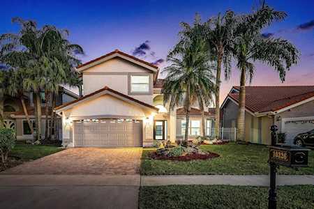 Two-story home with a lit double garage, palm trees, and a landscaped front yard at dusk.