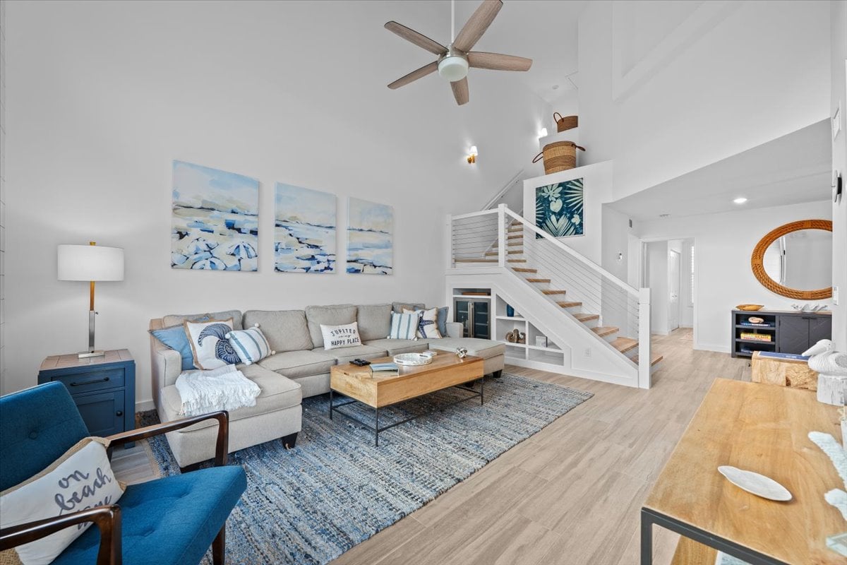 Furnished living room with a gray sectional, blue chair, vaulted ceiling, and open staircase.