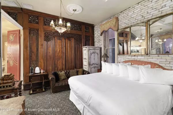 Bedroom with a large white bed, ornate carved wood paneling, and a white brick wall.