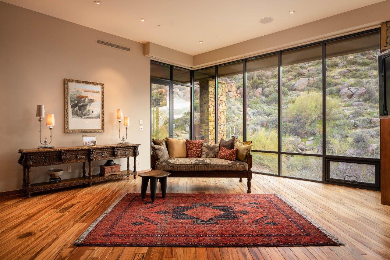 Living room with a patterned rug and sofa beside floor-to-ceiling windows overlooking a rocky hillside.