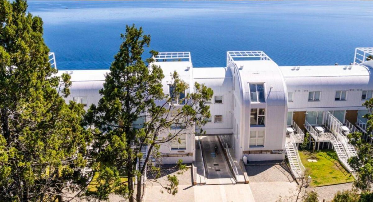 White apartment building with curved roof sections and balconies overlooking the ocean.