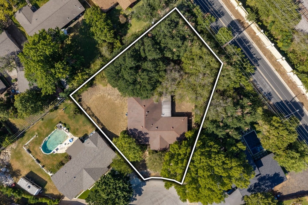 Aerial view of a wooded lot outlined in white, with a house near the bottom.